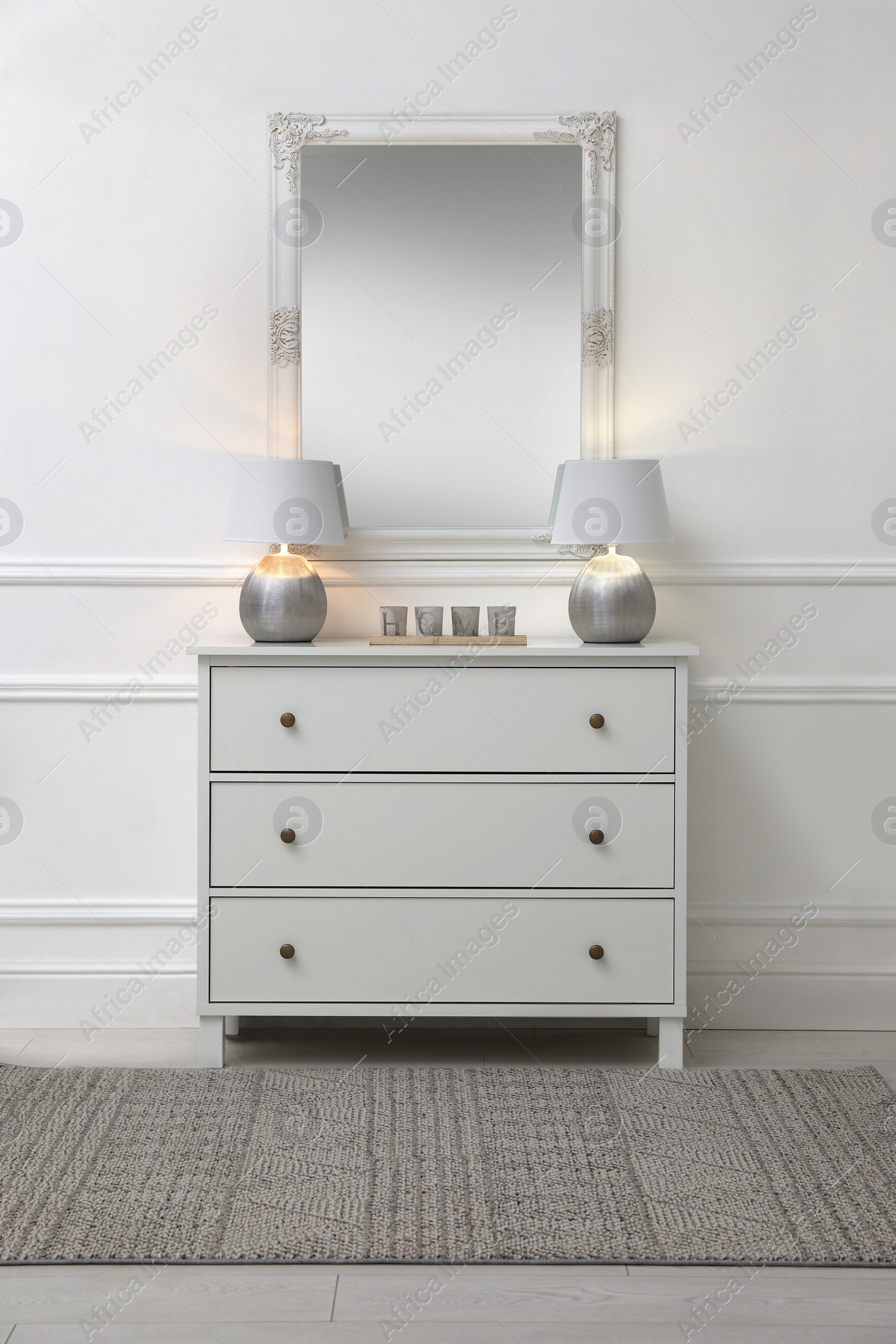 Photo of White chest of drawers with lamps near mirror in room. Interior design