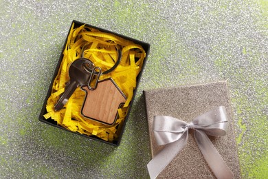 Key with trinket in shape of house, glitter and gift box on shiny surface, flat lay. Housewarming party
