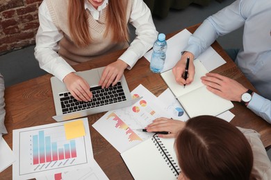 Team of employees working together at wooden table in office, above view