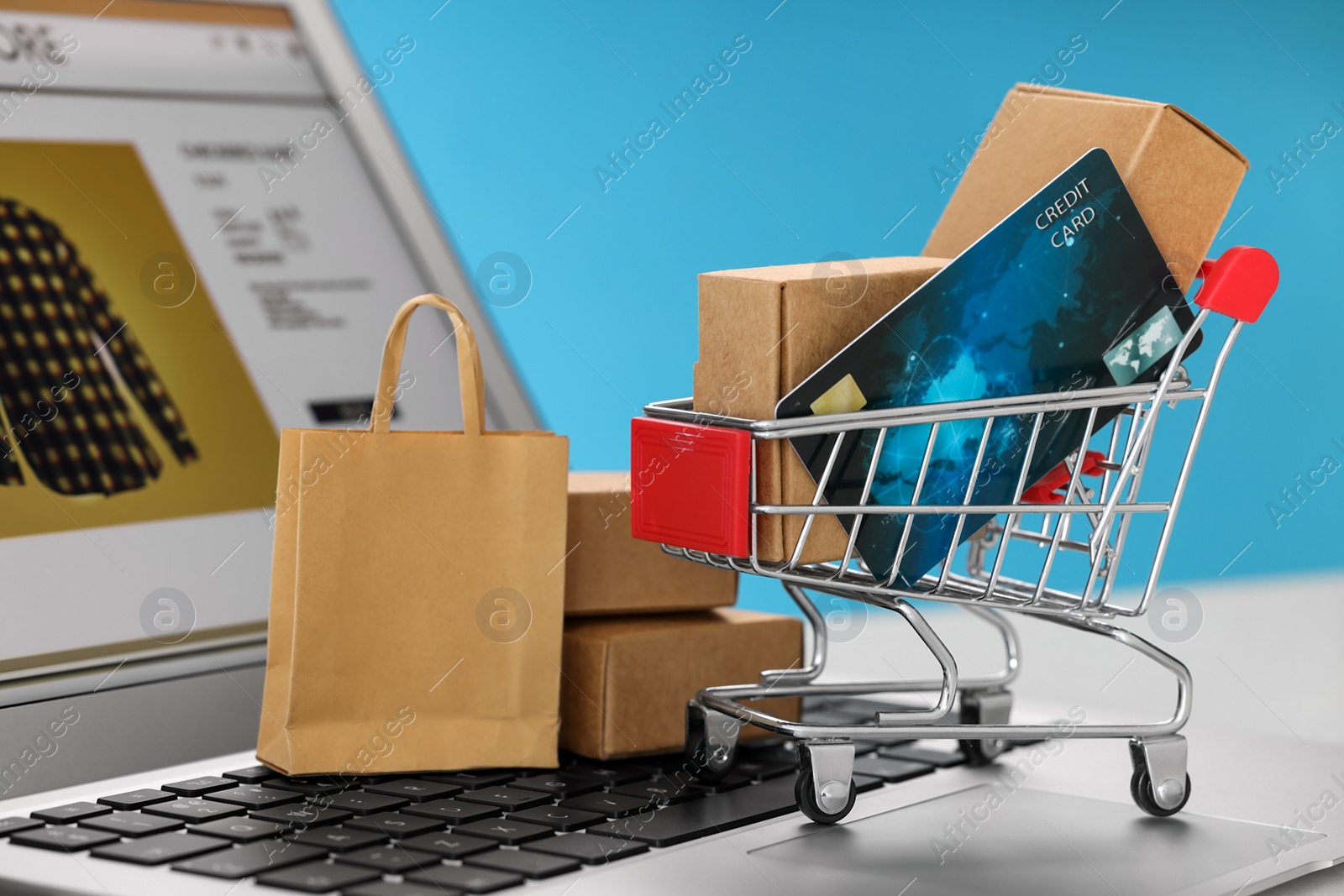 Photo of Mini boxes, credit card, cart and shopping bag on laptop against light blue background, closeup. Online store