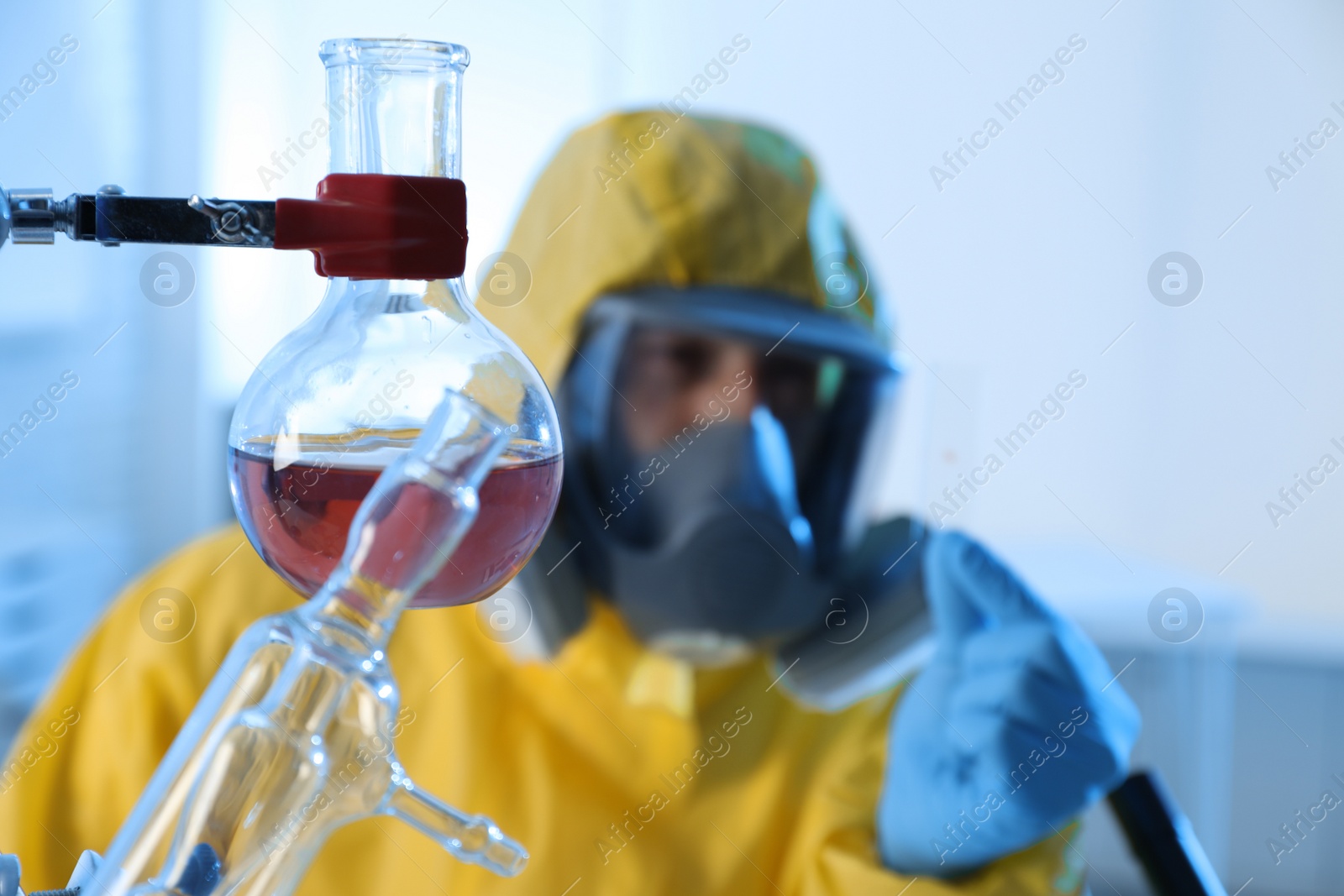 Photo of Flask with reagent and scientist in chemical protective suit working at laboratory. Virus research