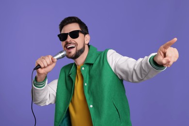 |Handsome man with sunglasses and microphone singing on purple background