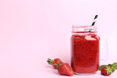 Photo of Tasty strawberry smoothie in mason jar on pink background. Space for text