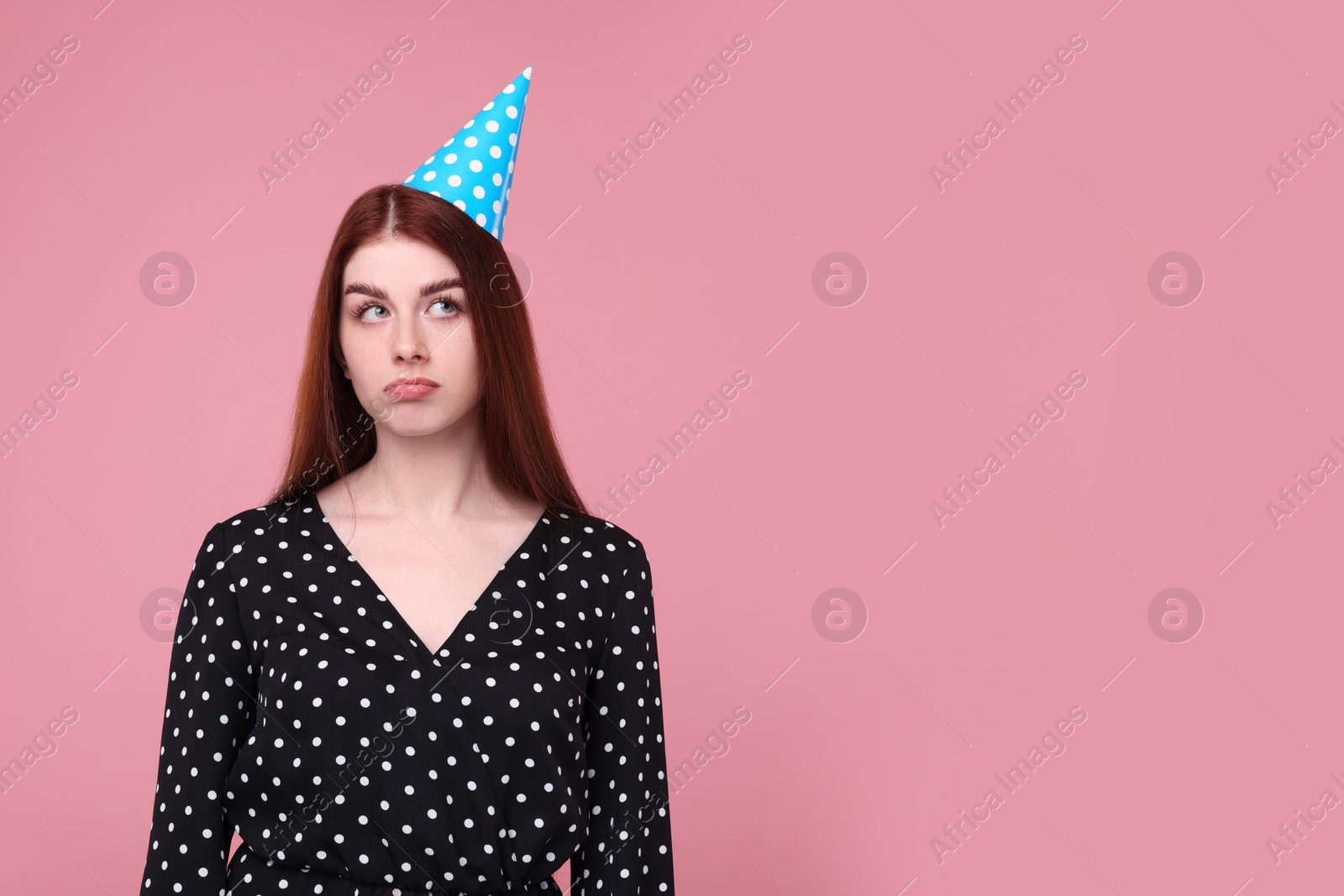 Photo of Sad woman in party hat on pink background, space for text