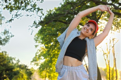 Photo of Young woman doing morning exercise in park. Space for text