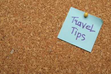 Photo of Colorful paper note with phrase Travel Tips pinned to cork board, closeup. Space for text