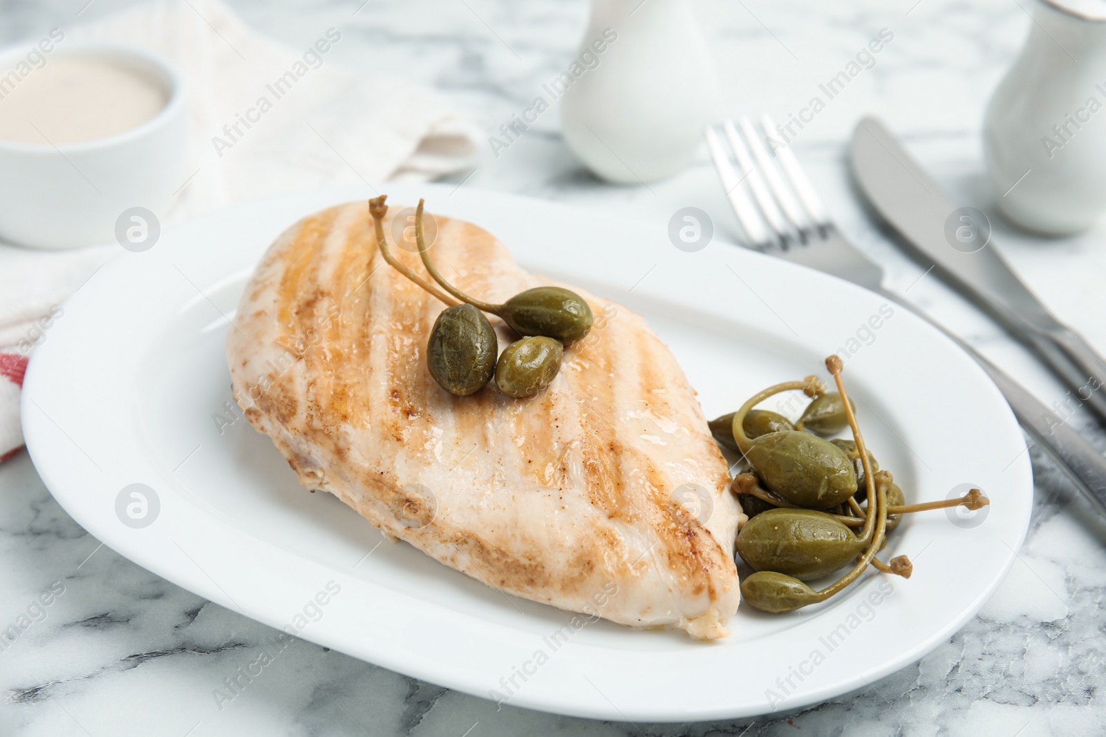 Photo of Delicious cooked chicken fillet with capers served on white marble table, closeup