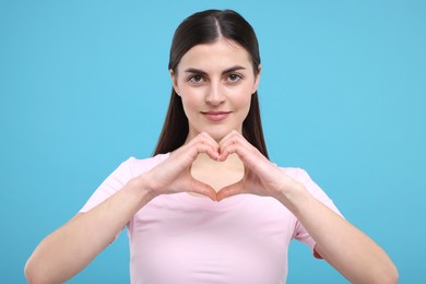 Photo of Beautiful young woman making heart with hands on light blue background