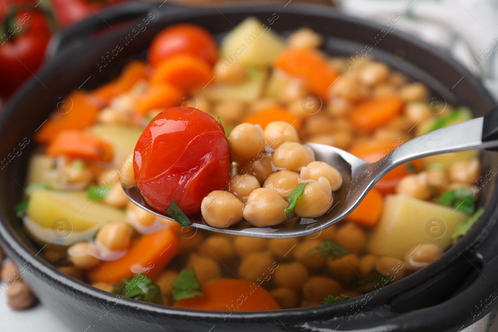 Photo of Taking tasty chickpea soup with spoon from bowl on table, closeup