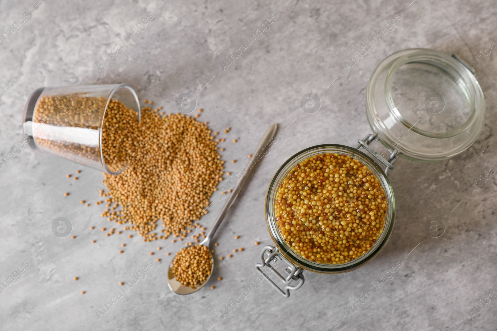 Photo of Delicious whole grain mustard and seeds on grey table, flat lay