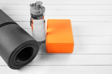 Photo of Exercise mat, yoga block and bottle of water on white wooden floor. Space for text