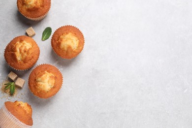 Photo of Delicious sweet muffins and brown sugar on light grey textured table, flat lay. Space for text