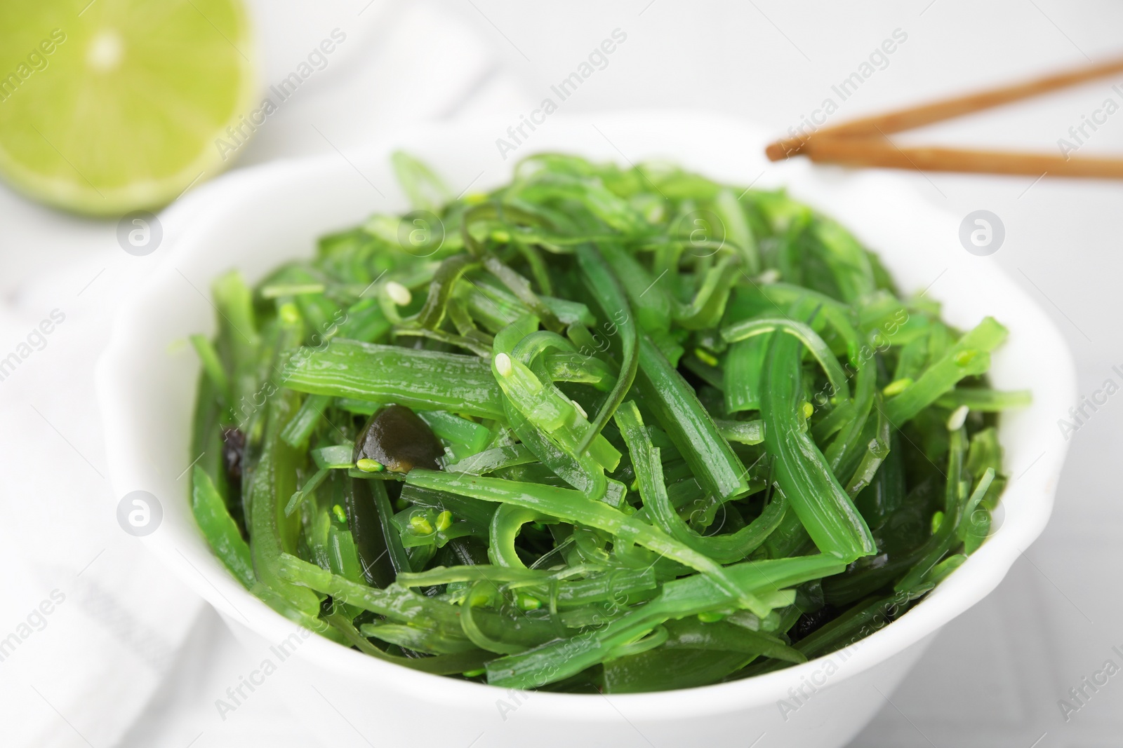 Photo of Tasty seaweed salad in bowl and chopsticks on white table, closeup