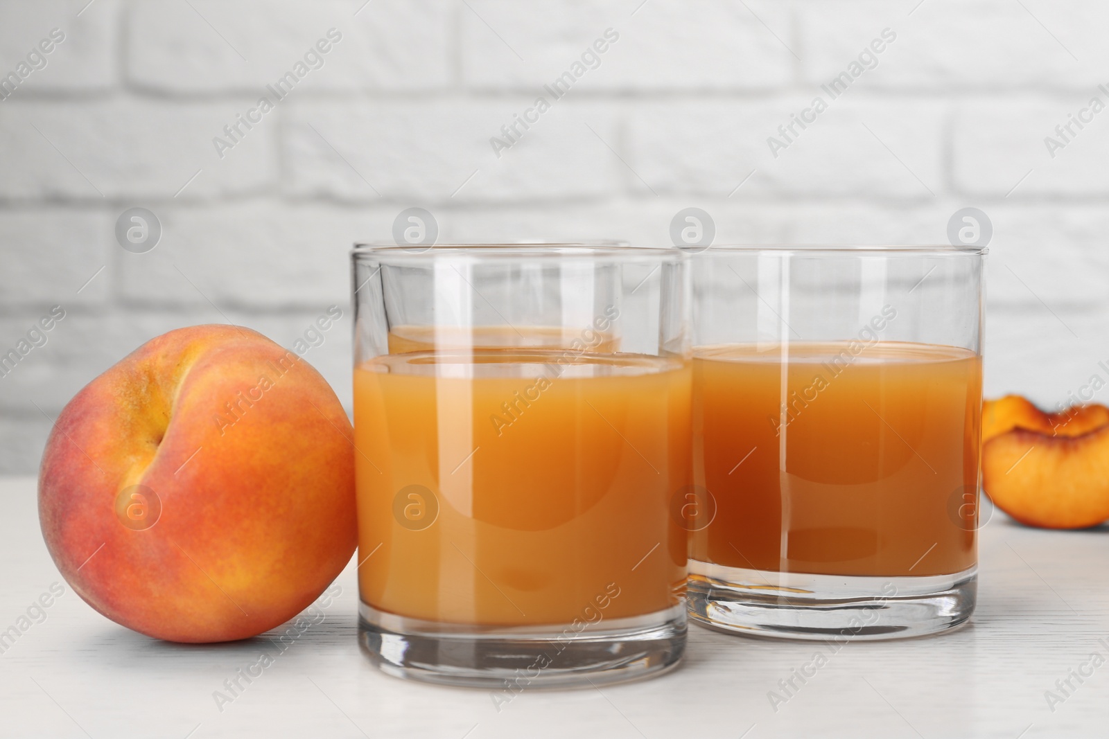 Photo of Glasses of delicious peach juice and fresh fruits on white wooden table