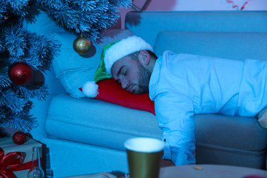 Drunk man wearing Santa hat sleeping on sofa after New Year party