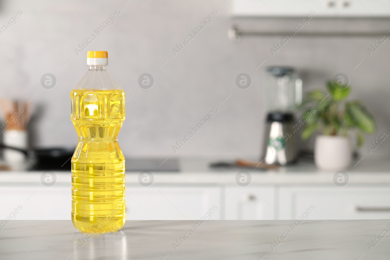 Photo of Bottle of cooking oil on white marble table in kitchen. Space for text