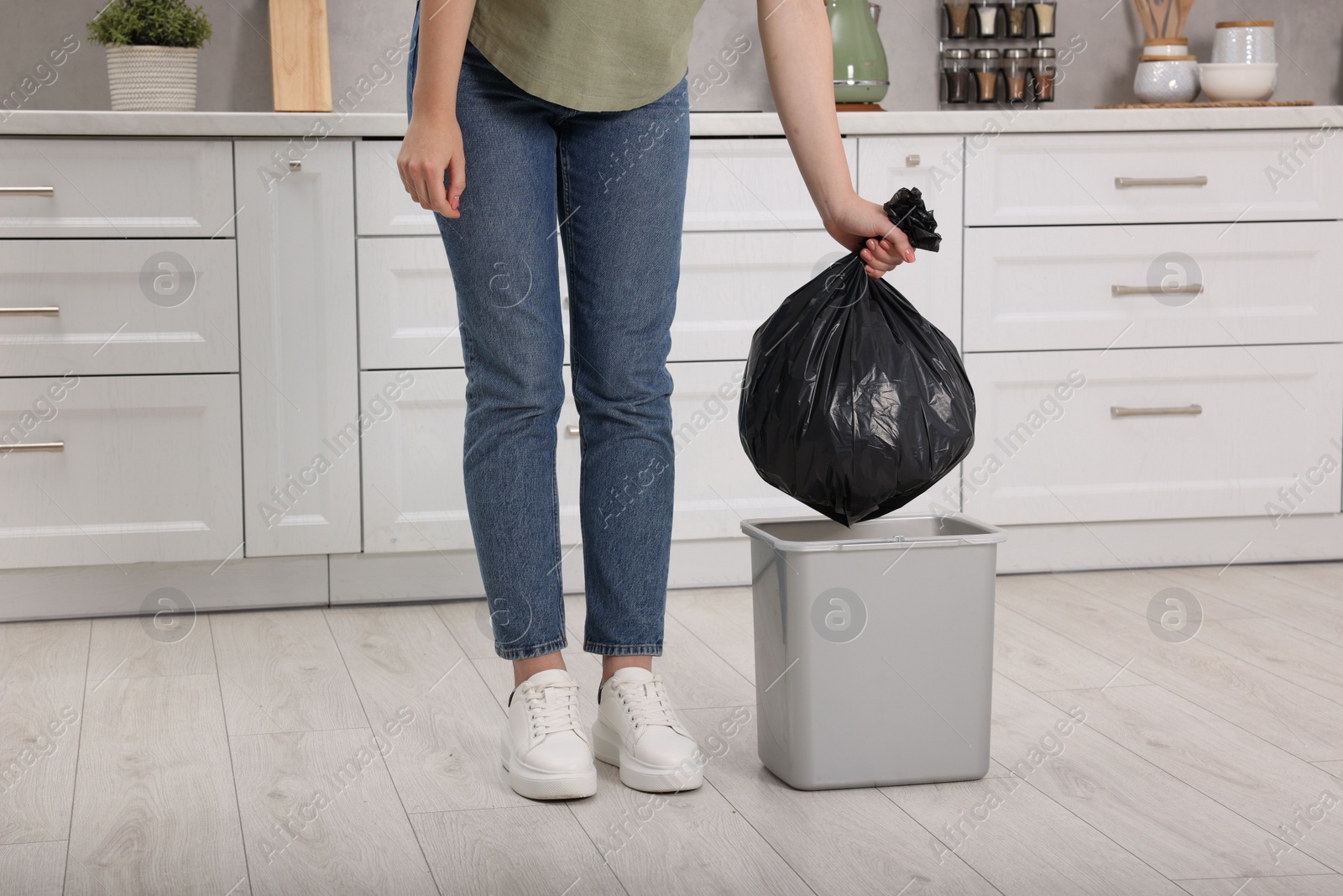 Photo of Woman taking garbage bag out of trash bin in kitchen, closeup