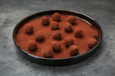 Photo of Delicious chocolate candies powdered with cocoa on grey table