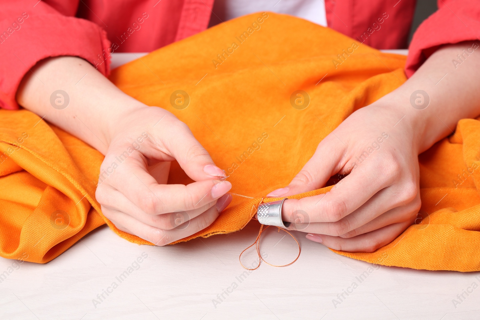 Photo of Woman sewing cloth with needle at light wooden table, closeup