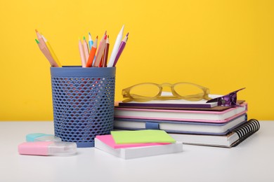 Photo of Different school stationery and glasses on white table against yellow background. Back to school