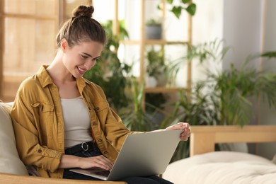 Photo of Happy young woman with laptop on armchair at home