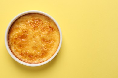 Delicious creme brulee in ceramic ramekin on yellow background, top view. Space for text