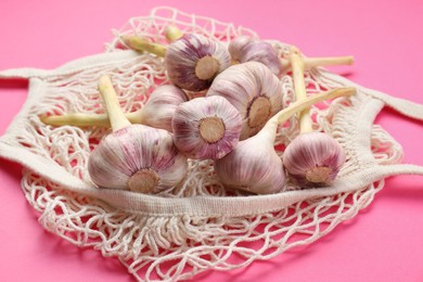 Photo of String bag with garlic heads on bright pink background, closeup