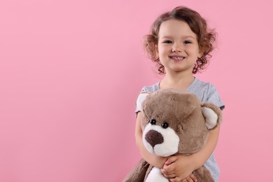 Cute little girl with teddy bear on pink background, space for text