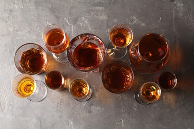 Different delicious liqueurs in glasses on grey table, flat lay