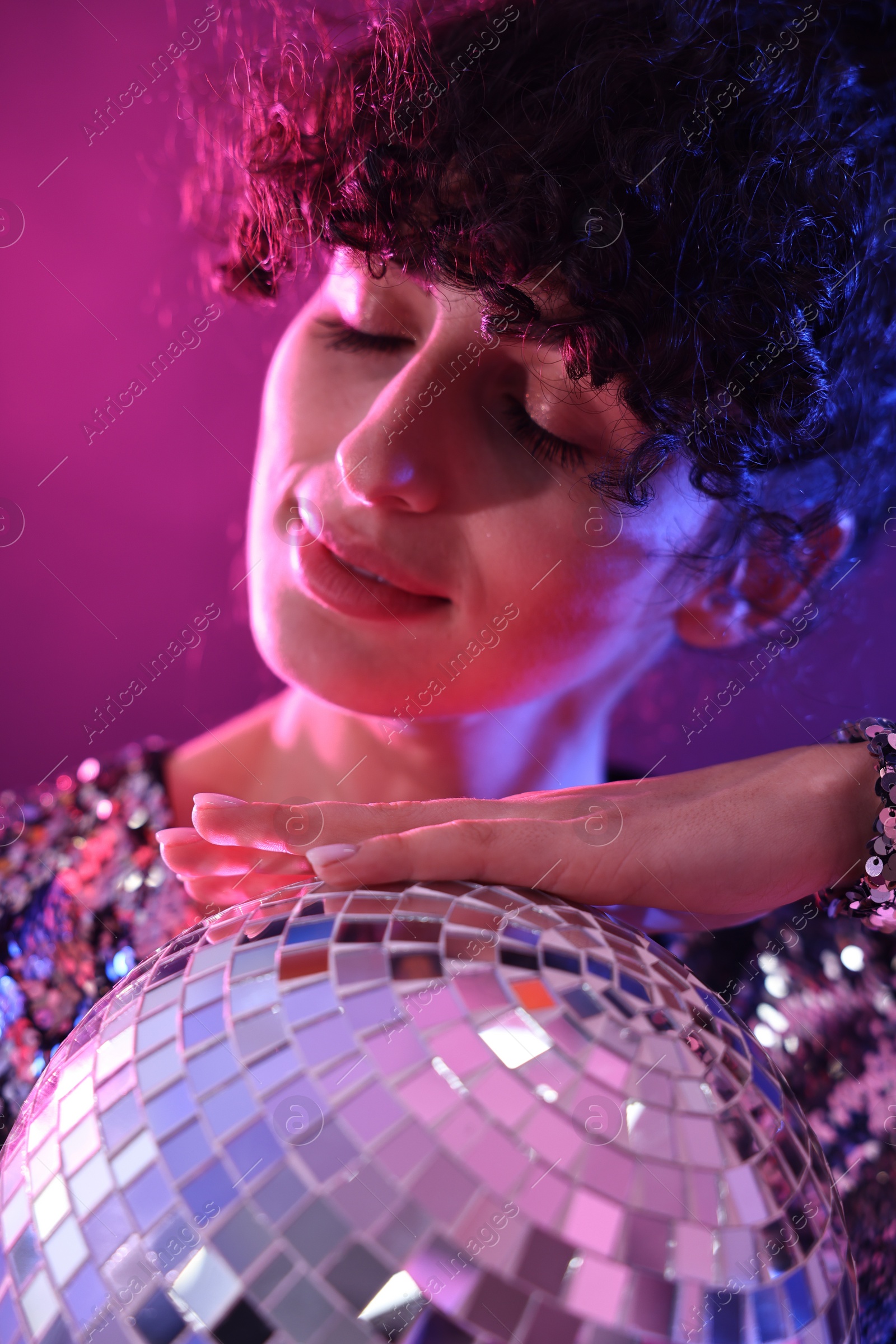 Photo of Beautiful young woman with disco ball posing on color background in neon lights, closeup