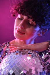 Photo of Beautiful young woman with disco ball posing on color background in neon lights, closeup