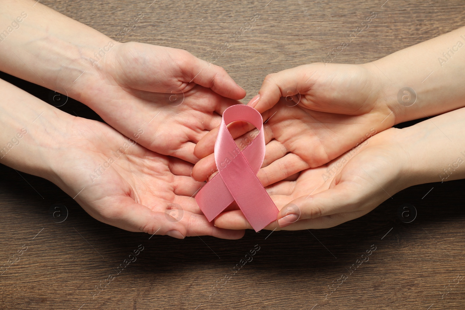 Photo of Women holding pink ribbon at wooden table, top view. Breast cancer awareness
