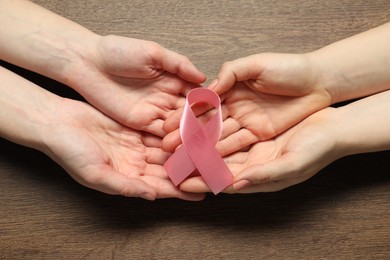 Women holding pink ribbon at wooden table, top view. Breast cancer awareness