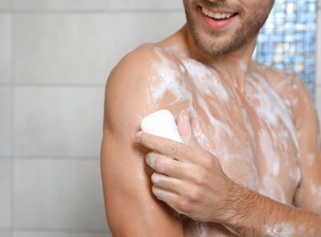 Photo of Young man taking shower with soap in bathroom, closeup. Space for text