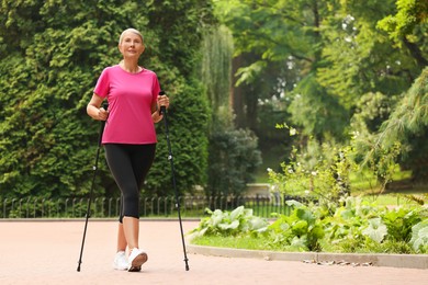 Senior woman performing Nordic walking outdoors, space for text. Low angle view