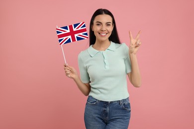 Image of Happy young woman with flag of United Kingdom showing V-sign on pink background