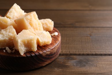 Photo of Pieces of delicious parmesan cheese on wooden table, closeup. Space for text