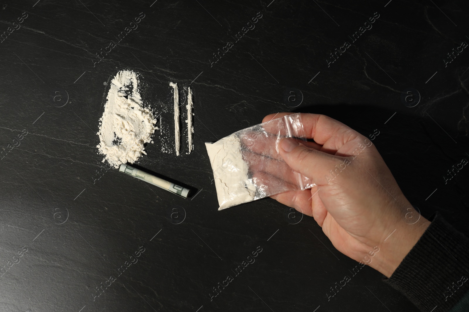 Photo of Drug addiction. Man with cocaine and rolled dollar banknote at dark textured table, top view