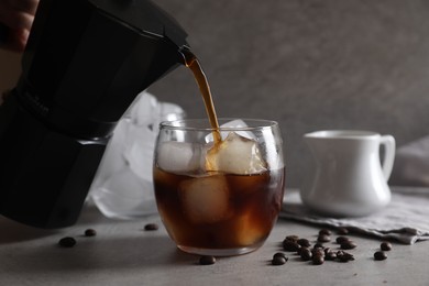 Woman pouring coffee into glass with ice cubes at gray table, closeup