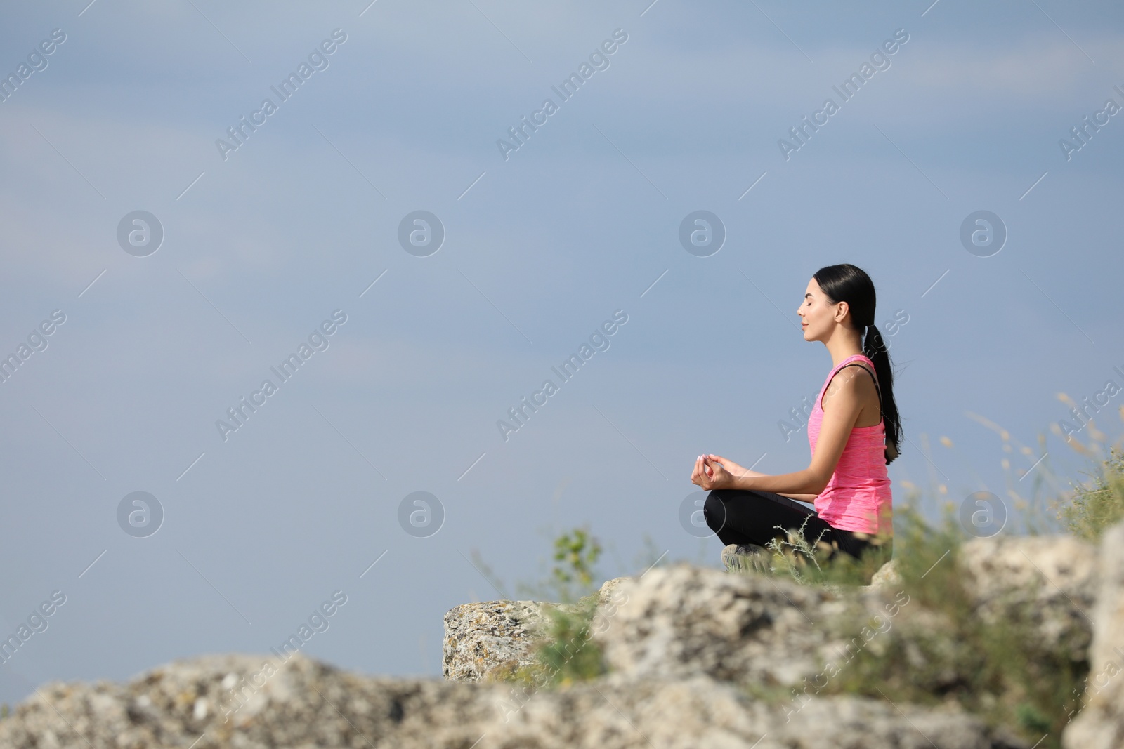 Photo of Young woman meditating on cliff. Space for text