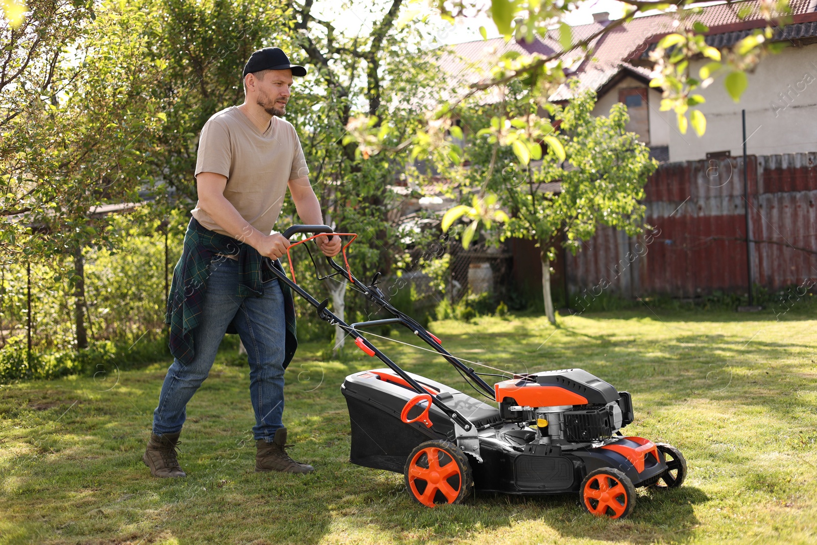 Photo of Man cutting green grass with lawn mower in garden