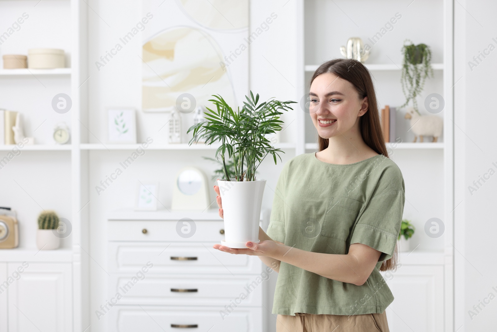 Photo of Beautiful young woman with green houseplant at home, space for text
