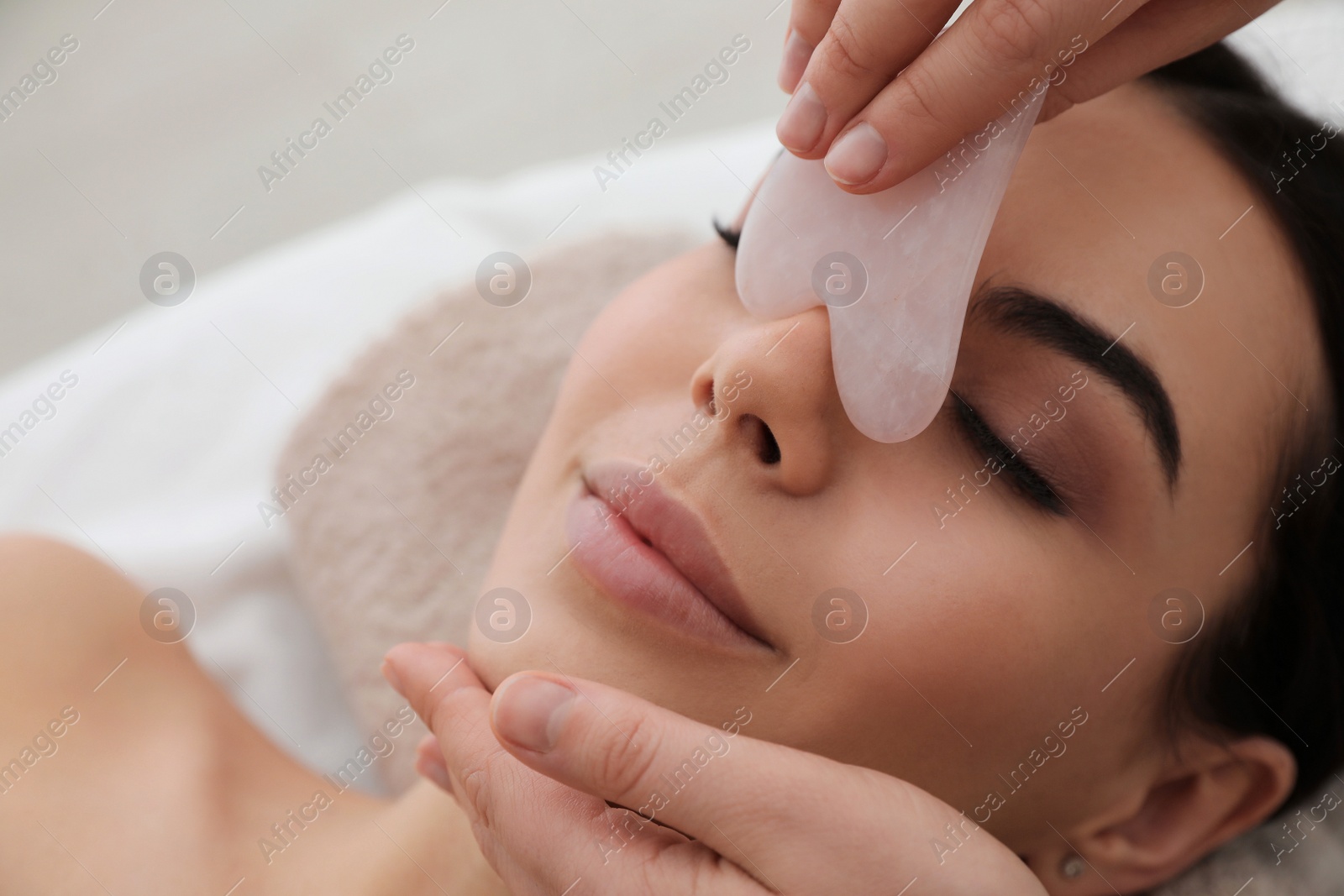 Photo of Young woman receiving facial massage with gua sha tool in beauty salon, closeup