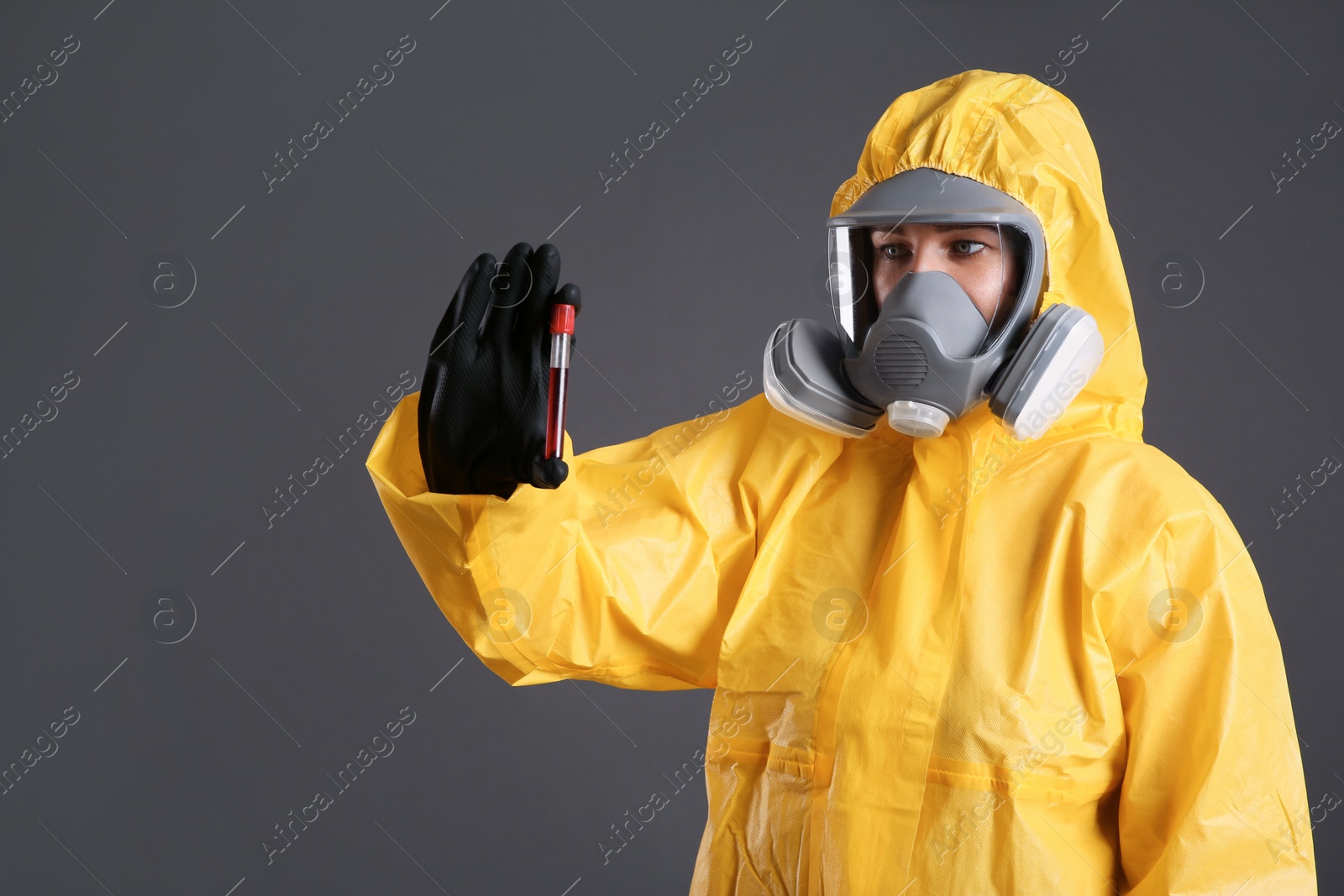 Photo of Woman in chemical protective suit holding test tube of blood sample on grey background. Virus research