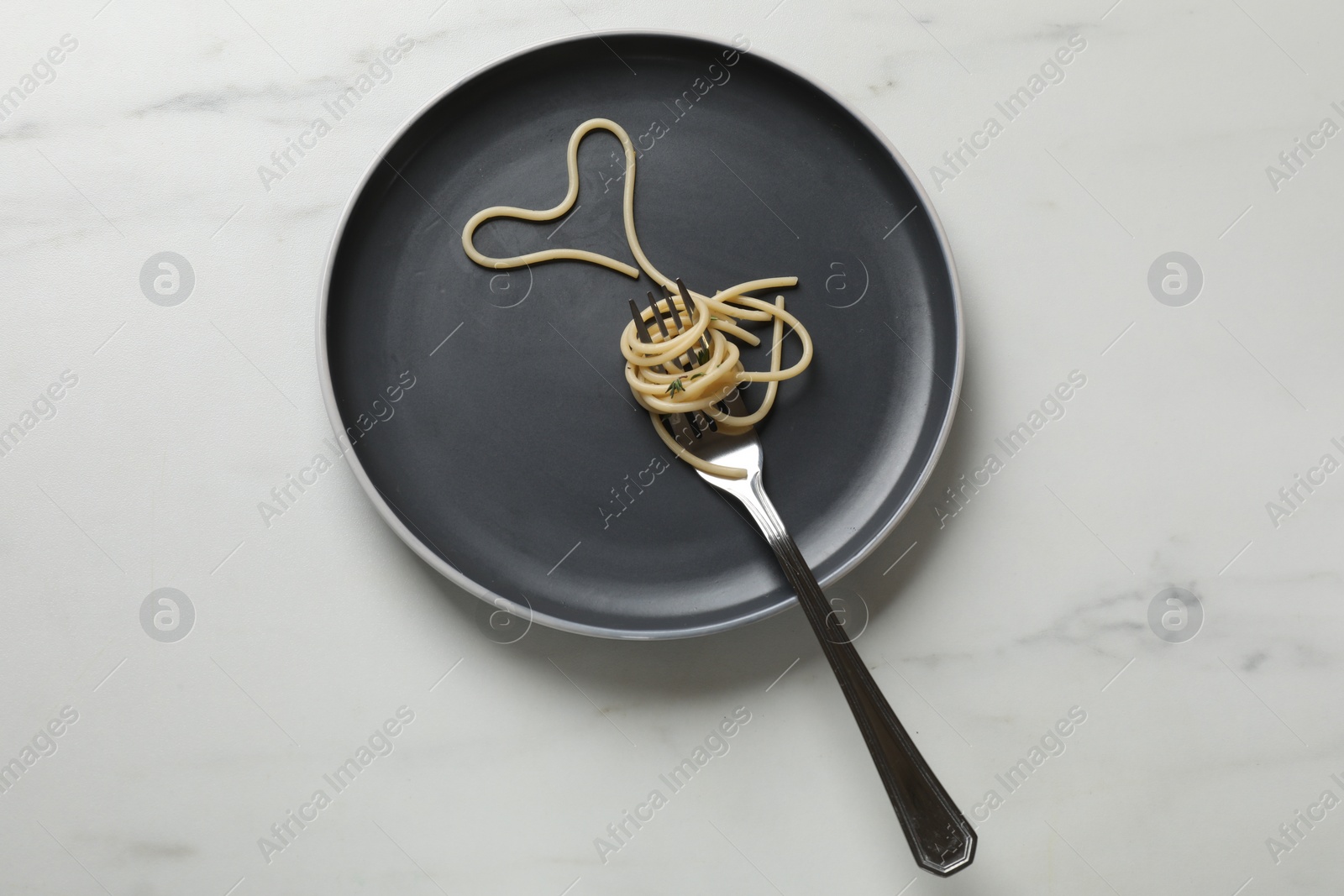 Photo of Heart made of tasty spaghetti and fork on white marble table, top view