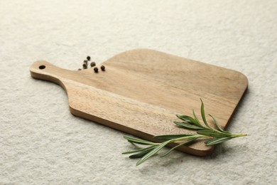 Photo of Cutting board, pepper and rosemary on white textured table. Space for text