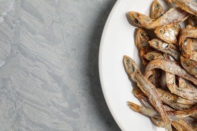 Plate of tasty dried anchovies on light grey marble table, top view. Space for text