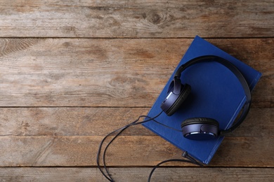 Modern headphones with hardcover book on wooden table, top view. Space for text