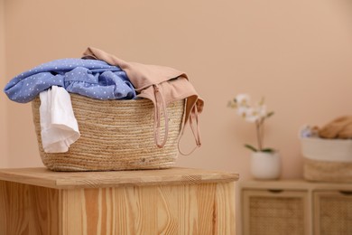 Photo of Wicker laundry basket overfilled with clothes on wooden table indoors. Space for text
