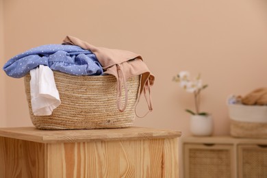 Wicker laundry basket overfilled with clothes on wooden table indoors. Space for text